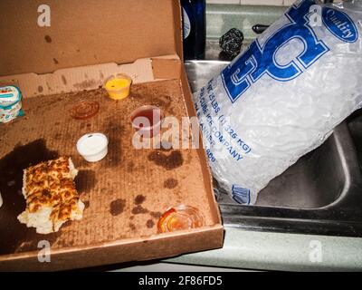 La vecchia pizza mangiata a metà ha lasciato sopra dopo una festa selvaggia in una casa disordinata, scattata in stile flash-on-camera. Foto Stock
