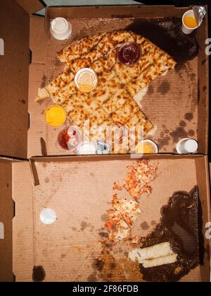 La vecchia pizza mangiata a metà ha lasciato sopra dopo una festa selvaggia in una casa disordinata, scattata in stile flash-on-camera. Foto Stock