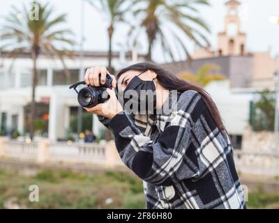 Giovane spagnola con una maschera nera e un la camicia a scacchi scatta foto all'aperto Foto Stock