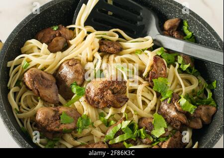 Fegato di pollo cotto con cipolla e spaghetti su una penna da cucina con prezzemolo. Gustosa cena di famiglia. Foto Stock