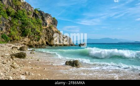 Onde sfocate in movimento che si infrangono su una spiaggia rocciosa appartata nell'area turistica tropicale di Puerto Galera sull'Isola di Mindoro nelle Filippine. Foto Stock