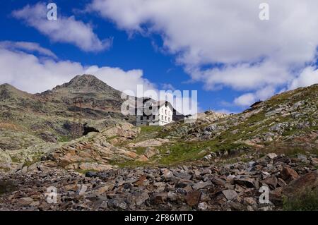 Una casa bianca isolata nelle Alpi italiane con montagne e nuvole sullo sfondo (Trentino, Italia, Europa) Foto Stock
