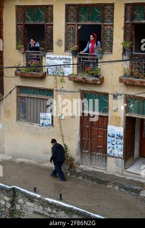 Due Signore che si affaccia da una finestra di una pensione e l'uomo anziano cammina nel villaggio storico Masuleh, Gilan Provincia, Iran Foto Stock