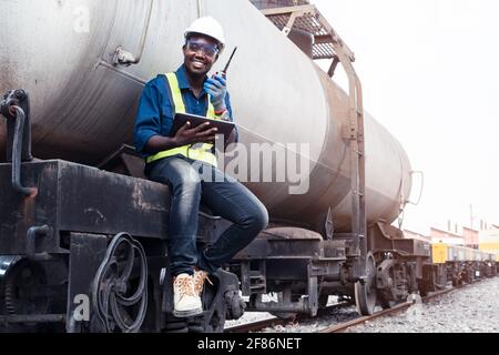 L'ingegnere africano maschile controlla un treno su ferrovia con parlare tramite comunicazione radio o walkie talkie con utilizzando tablet Foto Stock