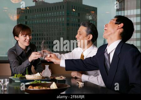 Felici uomini d'affari che brinda il sake nell'alto ristorante Foto Stock