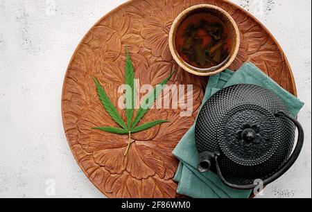 Teiera d'epoca con tè alle erbe alla cannabis e foglie di marijuana fresche allestite su sfondo concreto. Foto Stock