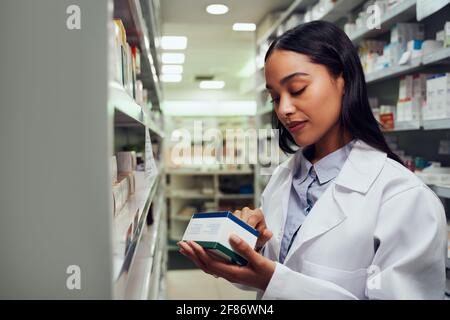 Giovane farmacista di sesso femminile che legge le istruzioni sulla scatola del medicinale in piedi dentro navata del chimico Foto Stock