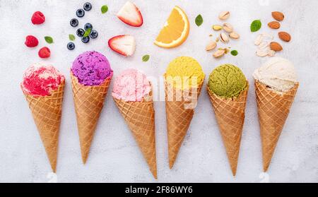 Varie di sapore di gelato in coni di mirtillo, pistacchio, mandorla, arancio e ciliegia impostazione su sfondo di pietra bianca. Menu estivo e dolce. Foto Stock