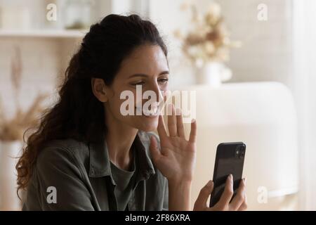 Primo piano donna sorridente che agita la mano sullo smartphone, videochiamata Foto Stock