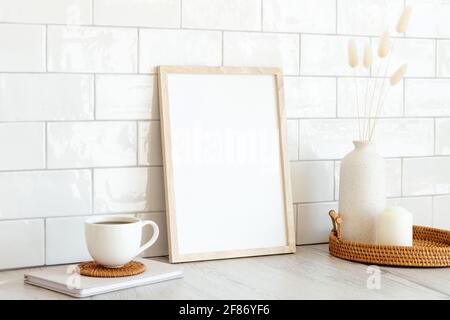 Mockup verticale bianco con cornice fotografica, tazza di caffè, vaso di fiori secchi, candela su tavolo di legno. Design nordico, scandinavo. Colazione Foto Stock