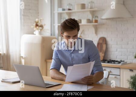 Uomo focalizzato che lavora con documenti, seduto a tavola con un computer portatile Foto Stock