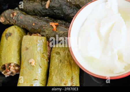 Zucchine farcite con carne tritata e riso. Presentazione di foglie ripiene (sarma yaprak) con yogurt, coltello, forchetta e cucchiaio su sfondo bianco. Foto Stock