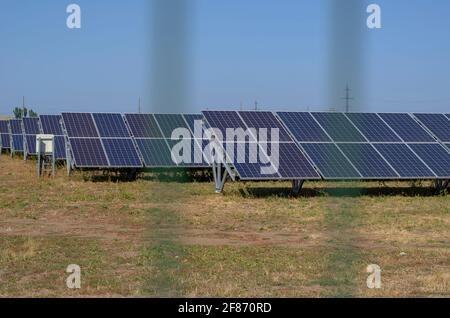 File di pannelli solari dietro una recinzione in un campo. Contorni sfocati della recinzione sullo sfondo della centrale solare. Energia rinnovabile. Messa a fuoco o Foto Stock