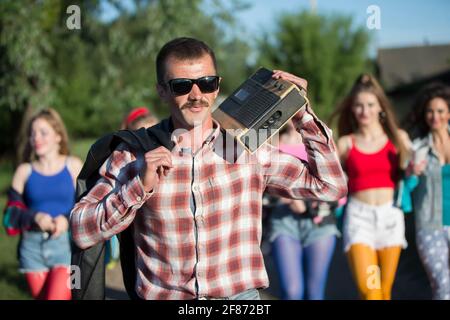 Uomo divertente con un registratore di cassette di fronte a un gruppo di ragazze. Persone nello stile degli anni novanta. Foto Stock