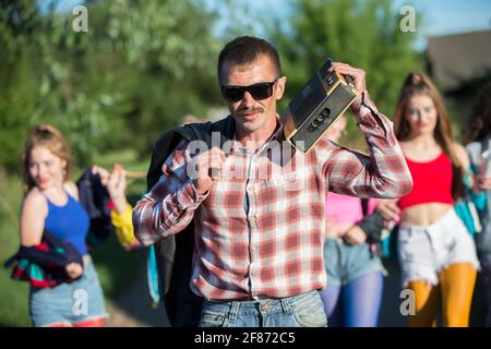 Uomo divertente con un registratore di cassette di fronte a un gruppo di ragazze. Persone nello stile degli anni novanta. Foto Stock