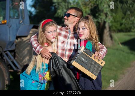 Uomo divertente con registratore di cassette abbraccia le ragazze. Persone nello stile degli anni novanta. Foto Stock