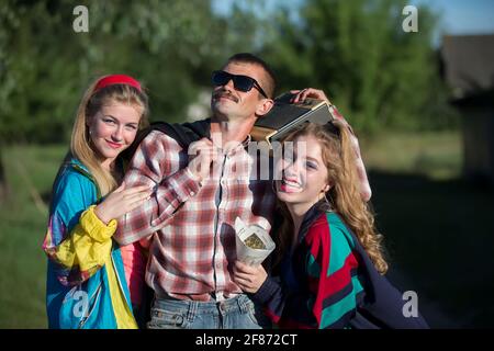 Uomo divertente con registratore di cassette abbraccia le ragazze. Persone nello stile degli anni novanta. Foto Stock