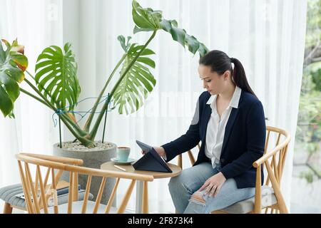 Bella giovane imprenditore femminile seduto al tavolo del caffè e la lettura articolo sul computer tablet Foto Stock