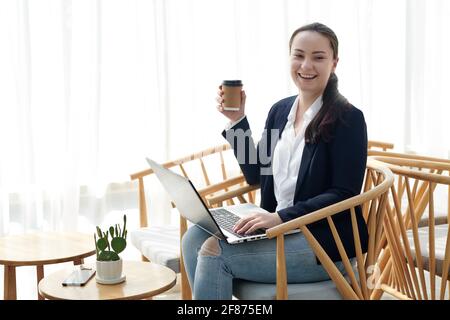 Felice ridendo giovane imprenditore femminile con computer portatile bere caffè in caffè Foto Stock