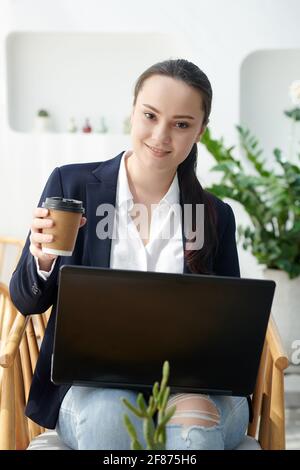 Sorridente prety univeristy studente che beve caffè e lavora su un computer portatile in caffetteria Foto Stock