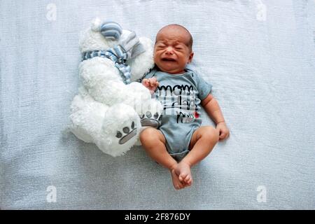 Piangendo bambino neonato. Bambino molto carino sul letto con grande giocattolo dell'orso Foto Stock