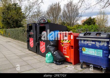 Una fila di contenitori di collezione di vestiti di beneficenza su una strada traboccante di donazioni Foto Stock