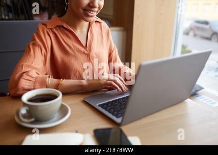 Ritratto troncato di giovane donna d'affari sorridente utilizzando il computer portatile mentre si gode il lavoro al tavolo da caffè, spazio di copia Foto Stock