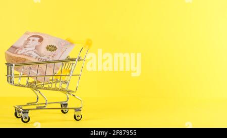 Carrello della spesa e mille note di baht thailandesi su uno sfondo giallo, primo piano. Acquisto del Black Friday e concetto di sconto Foto Stock