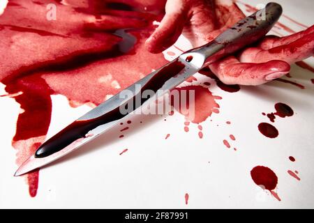 Una mano femmina sanguinosa tiene un coltello sanguinoso Foto Stock