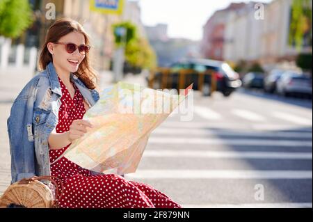 Donna sorridente che viaggia seduto a terra in città e utilizza la mappa su carta Foto Stock