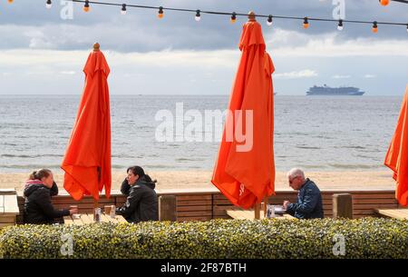 Bournemouth, Regno Unito. 12 aprile 2021. Desite il freddo, le persone che godono di un caffè in un caffè lungomare a Bournemouth, Dorset il giorno che i ristoranti, I pub e i caffè sono autorizzati a servire cibo e alcol ai clienti seduti all'esterno come parte della seconda fase della revoca delle restrizioni di blocco imposte durante il terzo blocco pandemico Covid-19 . Credit: Richard Crease/Alamy Live News Foto Stock