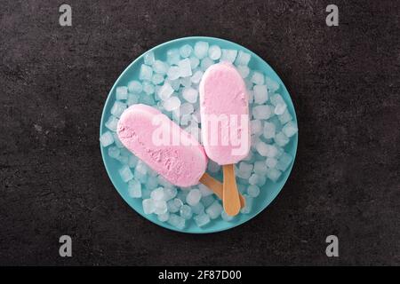 Popsicle di fragole e ghiaccio tritato su sfondo di ardesia nera Foto Stock