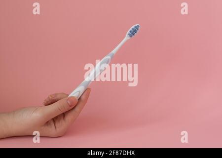 Spazzolino da denti in una mano della donna, igiene dentale, sfondo rosa Foto Stock