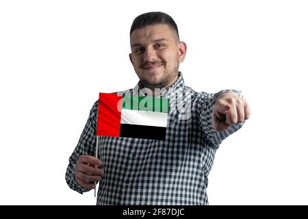 Ragazzo bianco che tiene una bandiera degli Emirati Arabi Uniti e punta in avanti davanti a lui isolato su uno sfondo bianco. Foto Stock