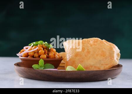 Colazione indiana  Poori con ceci chana masala curry, gustoso piatto indiano fatto usando farina di grano di tutti gli scopi che è disposto in una piastra di legno con Foto Stock