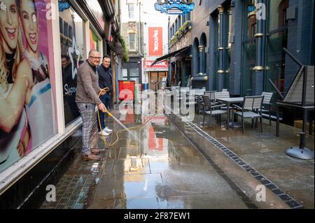 Cambridge, Regno Unito. 12 Aprile 2021. Il personale pulisce il marciapiede e l'area salotto fuori dal pub Town and Gown mentre i locali di ospitalità riaprono a Cambridge come parte del Regno Unito allentamento di Covid 19 restrizioni di blocco. La roadmap consente di usufruire di servizi esterni in pub e bar da oggi. Credit: Julian Eales/Alamy Live News Foto Stock