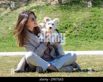 Giovane donna seduta a terra nel campo, trascorrendo del tempo con il suo cucciolo di schnauzer bianco. Foto Stock