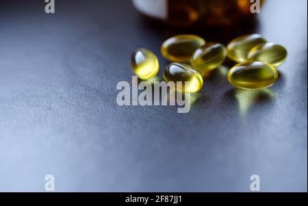 Pillole di medicina gialla in primo piano su uno sfondo nero con il loro contenitore in background. Foto Stock