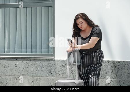 Donna piuttosto giovane che usa l'applicazione su smartphone quando si ordina un taxi auto per la stazione ferroviaria o l'aeroporto Foto Stock
