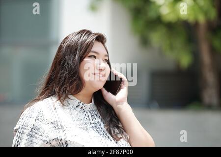 Bella bruna sorridente misto-razza stangig sulla strada della città e parlare al telefono con il marito Foto Stock