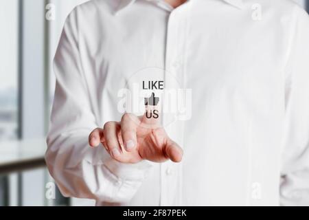 La mano dell'uomo d'affari preme sulla parola come noi con un'icona del pollice in su su su un touch screen virtuale. Concetto di marketing di popolarità dei social media aziendali. Foto Stock