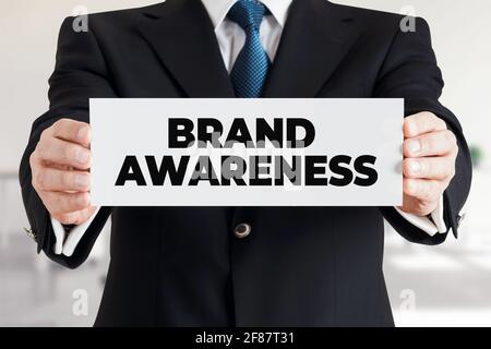 Uomo d'affari mostra un banner con il messaggio brand awareness. Concetto di branding della strategia di marketing aziendale. Foto Stock