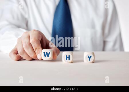 Mano di un uomo d'affari che mette i cubetti di legno con la domanda perché. Domande di approfondimento nel business. Foto Stock