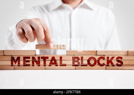 L'uomo d'affari costruisce una struttura di blocchi di legno con la parola blocchi mentali. Mancanza di attenzione o soppressione incontrollabile o repressione dei pensieri. Foto Stock