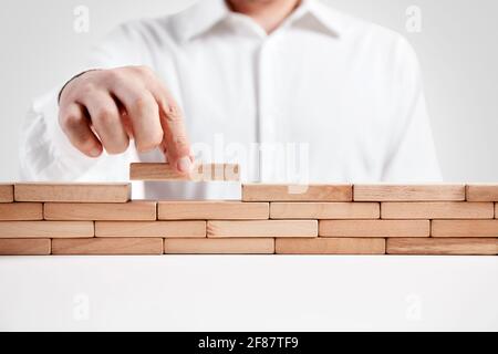 Uomo d'affari costruisce una barriera di blocchi di legno. Concetto di sicurezza, difesa o ostacoli. Foto Stock