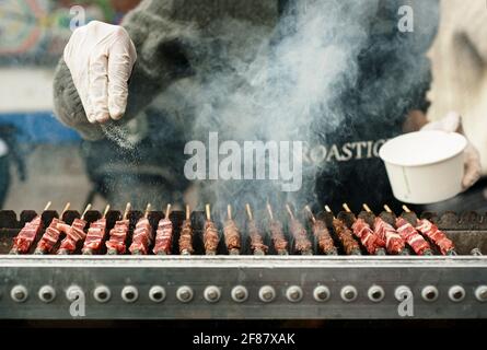 Primo piano degli spiedini in stile kebab per la salatura delle mani. Tostatura di carne su una macchina barbecue in un pop-up mercato alimentare. Brick Lane, Londra, Regno Unito. Apr 2014 Foto Stock