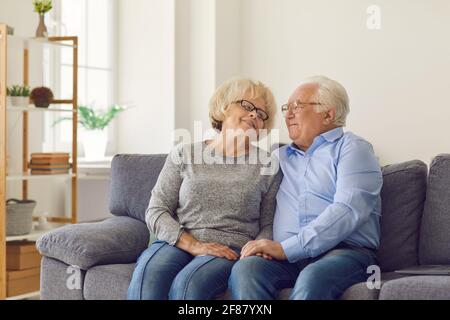 Felice coppia anziana affettuosa abbracciare e guardare l'un l'altro mentre si siede sul divano a casa. Foto Stock