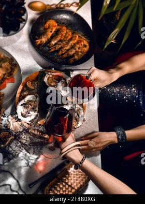 Primo piano di tavola nel ristorante di pesce servito con gamberi, ostriche, pesce di langoustina e le mani delle donne che tengono i bicchieri Foto Stock