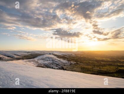 Splendida alba dorata sulla collina innevata montagna MAM Tor nel Derbyshire Peak District campagna incredibile cielo nuvoloso paesaggio. Scena invernale senza persone Foto Stock