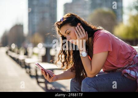 Triste giovane donna è seduta su panchina in città. È depressa. Foto Stock